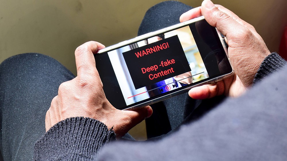 Man holding phone with deepfake content warning on screen