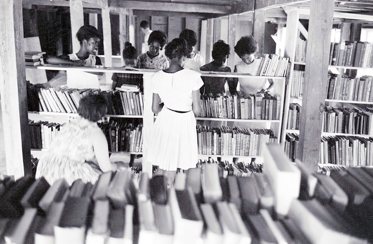 A white volunteer and Black female students browse the shelves of a library room at the Canton Freedom Community Center in Mississippi in July 1964.