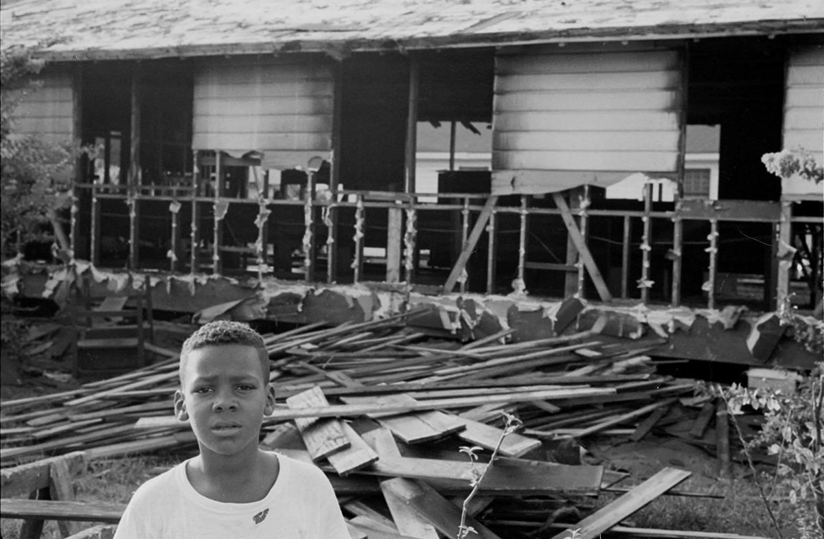 A young boy stands outside a burned-out church in Mississippi, a pile of rubble behind him, during Freedom Summer in July 1964.