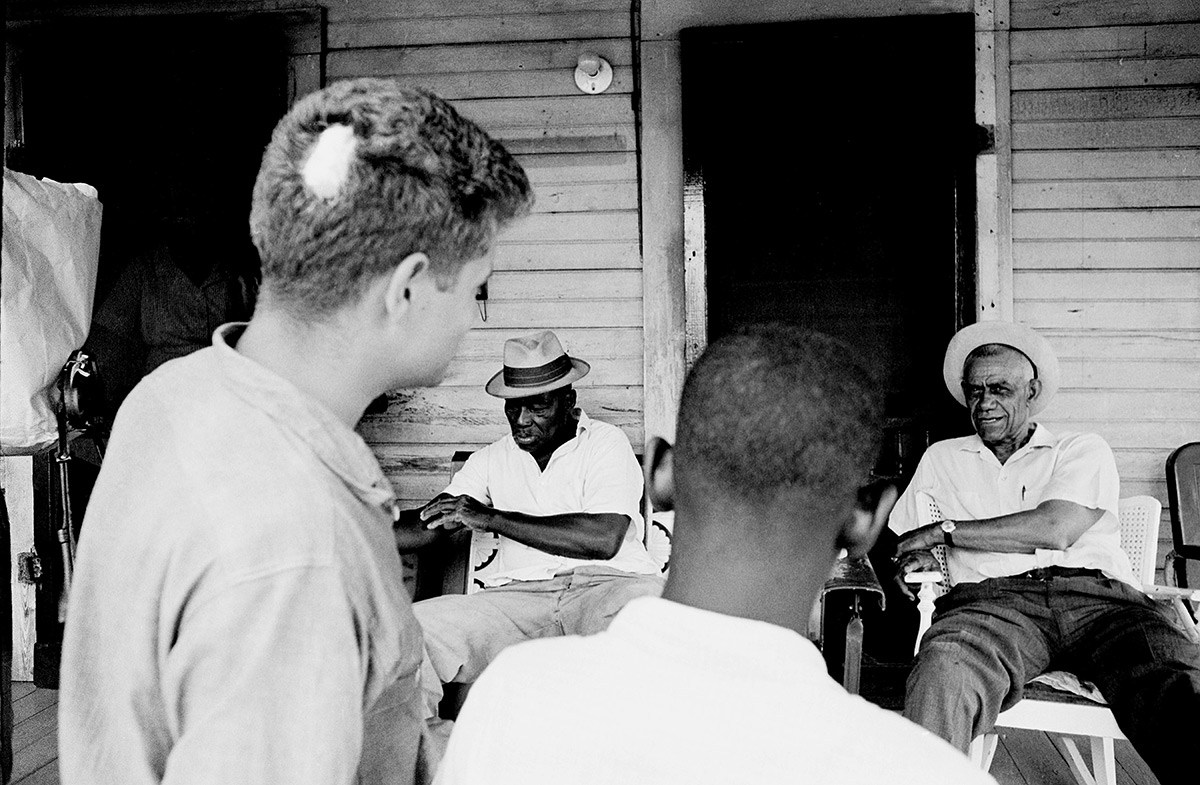 Freedom Summer 1964 volunteer David Owen and a volunteer speak to two men about voter registration on the porch of a home. A patch of hair is missing from Owen's head from being attacked.