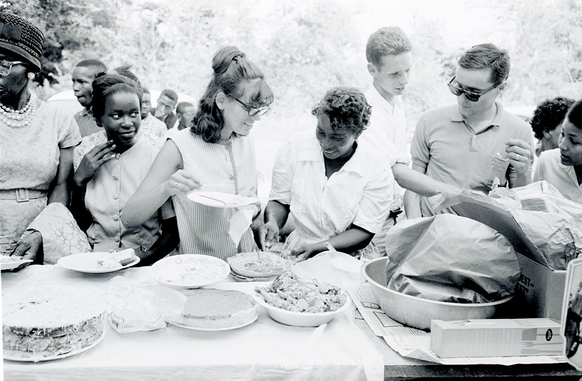 Volunteers with the Student Nonviolent Coordinating Committee stand near a table of food at a picnic in July 1964.