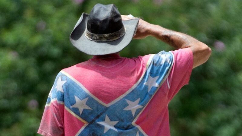 Man wearing Confederate flag shirt and cowboy hat saluting