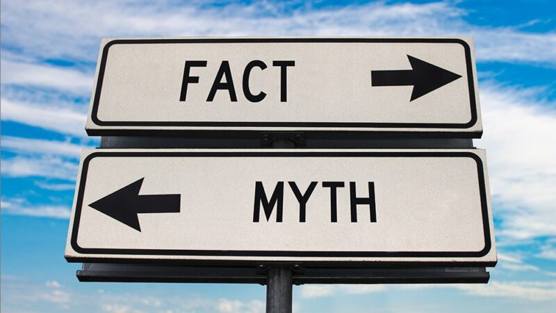 Fact versus myth road sign with two arrows on blue sky background.