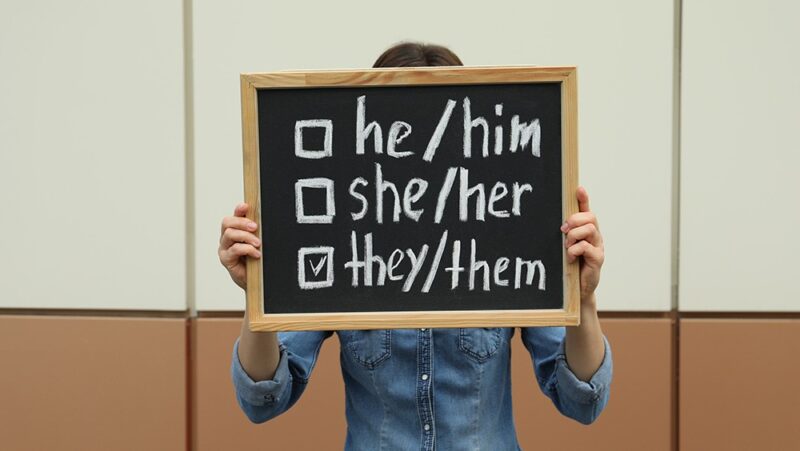 Woman holding chalkboard with list of gender pronouns