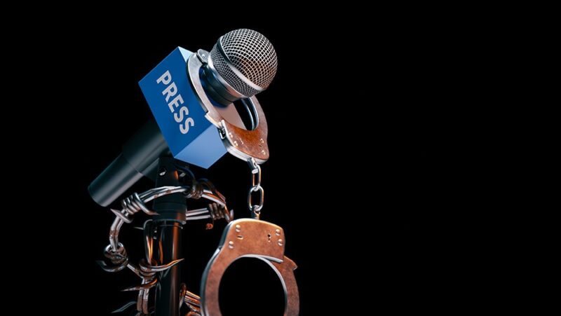 Journalist microphone with word press written on it wrapped in handcuffs and barbed wire.