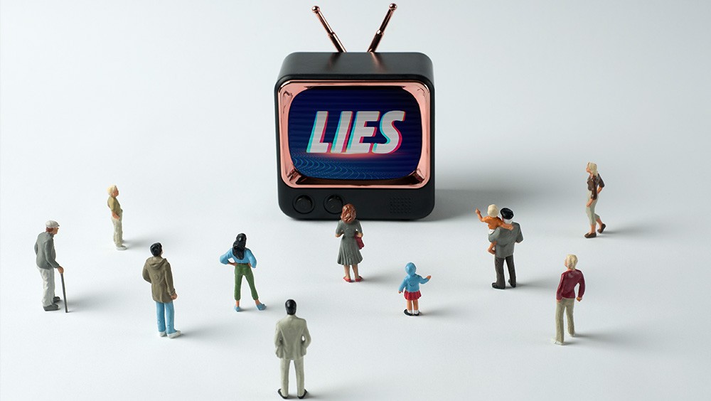 Figurines watching TV with word "lies" on screen.