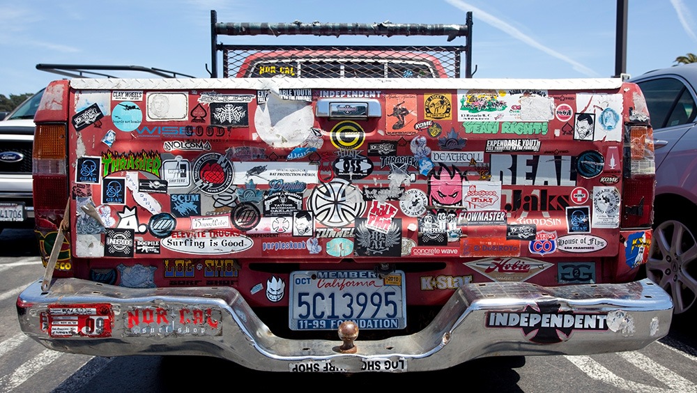 Rear of red pickup truck covered in bumper stickers.