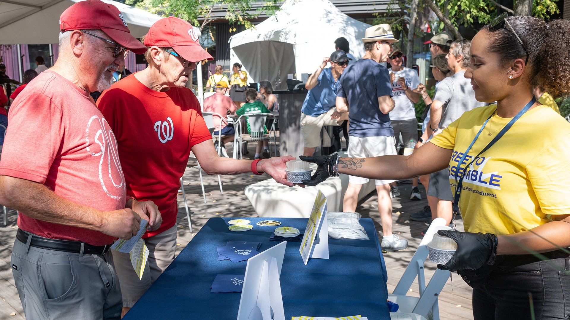 Two guests in Washington Nationals T-shirts and baseball caps get cups of Speak Your Mud ice cream from a 1A Fest staffer.