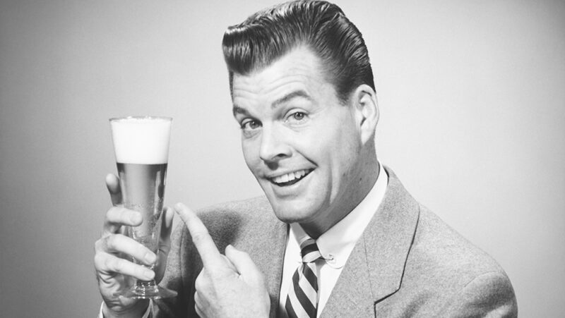 Businessman in full suit in studio pointing at glass of beer