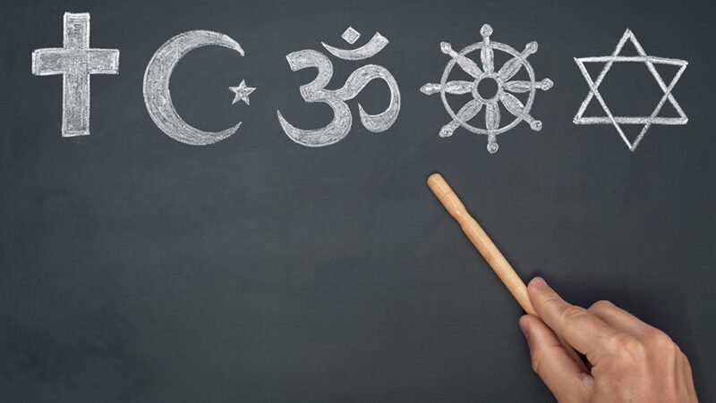 Concept of religion being taught in school showing major religious symbols on chalkboard with hand holding pointer stick